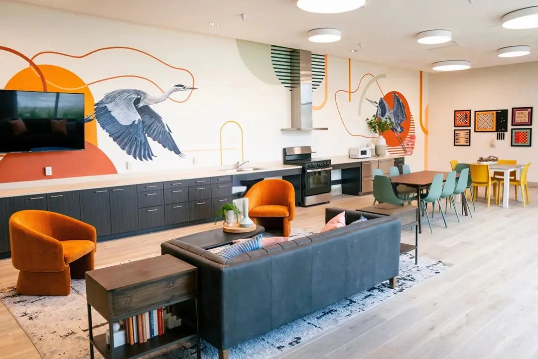 Main Street Apartments lounge with a heron mural, navy sofa and orange chairs